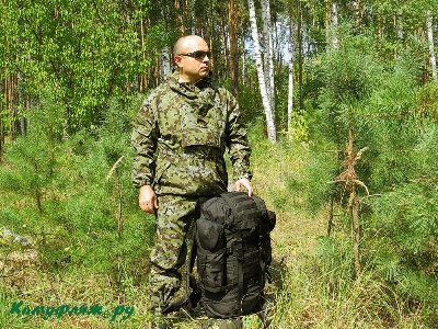На фото малый рейдовый рюкзак на 65 литров – черный. Зеленый летний ландшафт.